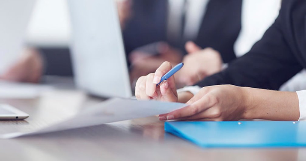 Close-up of hands holding a pen and paper at a desk.